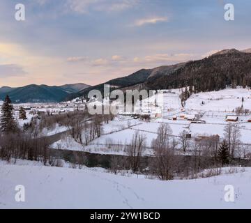 Lo spuntar del giorno mattina inverno tramonto dei Carpazi villaggio di montagna Zelene in nero Cheremosh river valley tra alp. Vista dalla campagna coperta di neve percorso sulla collina Foto Stock