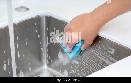 Strofinare un lavandino della cucina con acqua saponata utilizzando una spugna sotto l'acqua corrente. Foto Stock