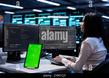 Scienziati informatici nei data center che controllano le prestazioni delle apparecchiature su tablet con schermo verde dopo l'aggiornamento delle macchine. Amministratori che eseguono la manutenzione dei carri nella sala server utilizzando un dispositivo Chroma Key Foto Stock