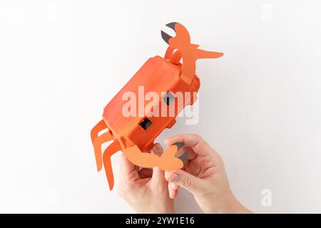 Progetto artigianale che assomiglia al granchio realizzato in cartone d'uovo dipinto di rosso con gambe di carta, artigli, sfondo bianco. Divertente idea di riciclaggio fai da te Foto Stock
