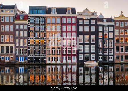 Gli iconici e stretti edifici fiancheggiano i canali di Amsterdam, creando una pittoresca vista autunnale. Le acque calme rispecchiano la loro bellezza mentre il crepuscolo inizia a stabilirsi nei Paesi Bassi Foto Stock