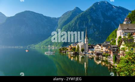 Annidato tra vette torreggianti, un pittoresco villaggio sul lago riflette il cielo azzurro, Hallstatt Austria Foto Stock