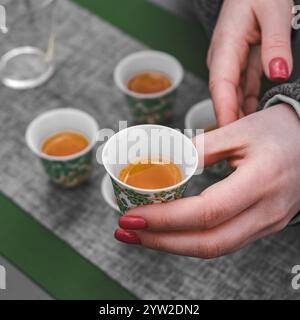 Le mani tengono in mano una tazza di tè alle erbe, con tazze decorative colorate sullo sfondo Foto Stock