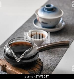 Una disposizione squisita che presenta una splendida teiera in vetro, tazze delicate e un ambiente tranquillo e sereno Foto Stock