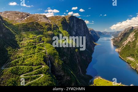 Una vista aerea di una strada tortuosa che serpeggia attraverso una lussureggiante valle verde, culminando al bordo di un meraviglioso fiordo in Norvegia. Lysebotn, Lysefjorden, Nor Foto Stock