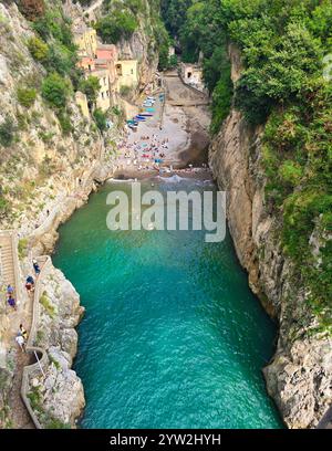 Bagnata dalla luce del sole, le acque cristalline riflettono la facciata colorata del Fiordo di Furore, la spiaggia di Furore, la costiera amalfitana Italia Foto Stock