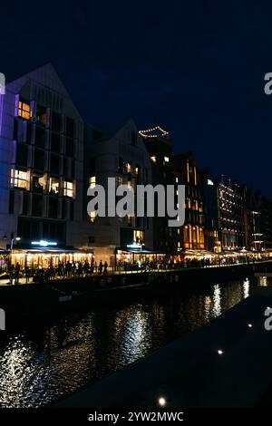 Vista notturna sul lungomare di edifici moderni illuminati e riflessi sul fiume Motlawa. Danzica, Polonia - 19 maggio 2024 Foto Stock