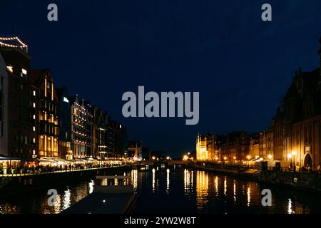 Vista notturna sul lungomare di edifici moderni illuminati e riflessi sul fiume Motlawa. Danzica, Polonia - 19 maggio 2024 Foto Stock