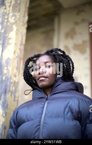 Giovane donna con i capelli intrecciati che indossa una giacca nera in piedi di fronte a una parete intemprata, Brandeburgo, Germania Foto Stock