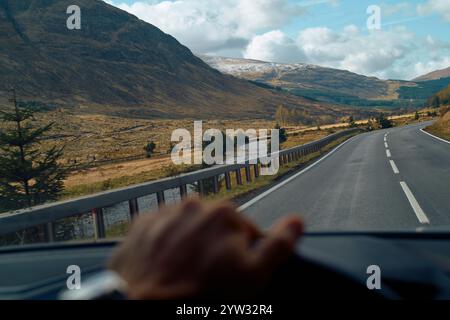 Paesaggio montano visto da un'auto con la mano del conducente al volante, Highlands, Scozia Foto Stock