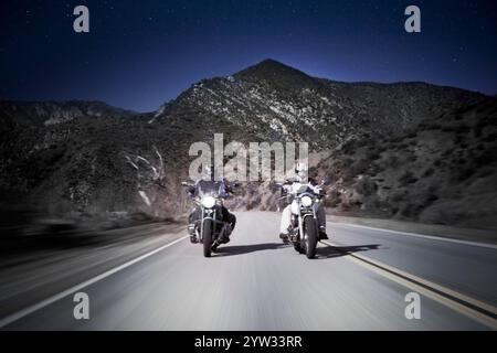 Due motociclette attraversano strade ventose di montagna di notte. Foto Stock