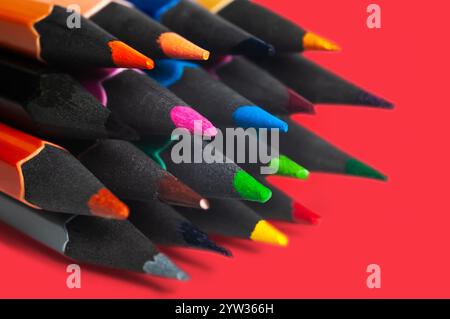 Foto dettagliata di matite colorate disposte su uno sfondo rosso brillante. Mette in risalto la creatività e i concetti artistici attraverso tonalità vivaci e Sha Foto Stock