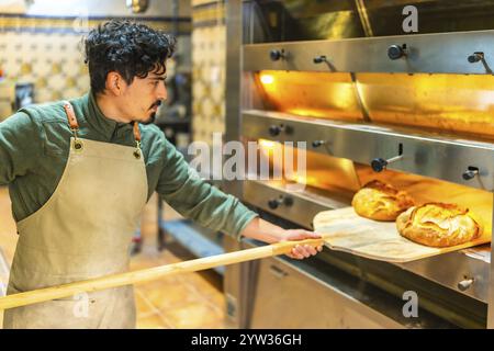 Giovane latino che cuoce il pane in un forno tradizionale utilizzando una buccia di legno Foto Stock