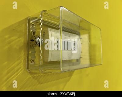 Un termostato con coperchio trasparente bloccabile su una parete gialla, che controlla le spese di riscaldamento. Foto Stock