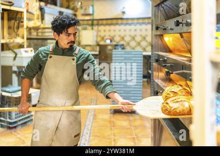 Giovane latino che usa una buccia di legno per rimuovere il pane dal forno tradizionale Foto Stock