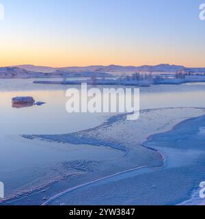Lago ghiacciato all'alba con ghiaccio sereno e neve che riflettono morbide mor Foto Stock