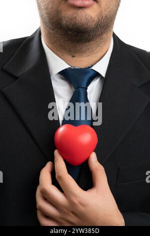 Uomo d'affari adulto che indossa una tuta da ufficio elegante e casual con cuore rosso vicino al petto come simbolo d'amore concetto di primo piano isolato su studi bianchi Foto Stock