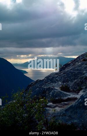I raggi del sole si infrangono tra le nuvole su un tranquillo paesaggio montano con uno sguardo sul mare, Romsdalfjorden, Norvegia Foto Stock