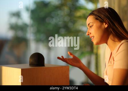 Profilo di una donna che parla con un altoparlante intelligente a casa Foto Stock