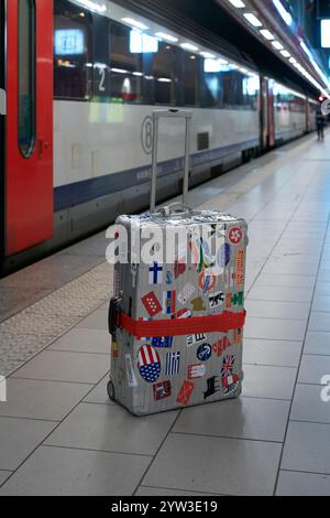 Una valigia ben viaggiata con adesivi internazionali si trova da sola su una piattaforma ferroviaria, Bruxelles, Belgio Foto Stock