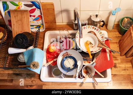 Un lavandino pieno di piatti sporchi e utensili da cucina dai disegni colorati, circondato da un ripiano in legno e da Backsplash, Germania Foto Stock