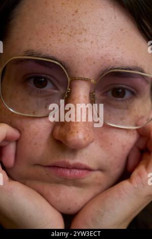 Ritratto ravvicinato di una donna lentigginata con occhiali rotondi che tiene delicatamente il viso con le mani, Dresda, Germania Foto Stock