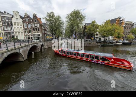 Vecchi edifici tradizionali del centro storico della città lungo il canale Keizersgracht con il ponte Leidsegracht e la barca turistica rossa per la crociera sul canale Foto Stock