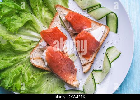 Panini con formaggio fresco e fette di trota salata su un piatto bianco con cetriolo ed erbe aromatiche. Foto di alta qualità Foto Stock