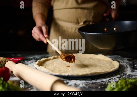 Un cuoco aggiunge i condimenti a un impasto fatto in casa per pizza in una cucina calda e invitante. La scena evoca un senso di calore e creatività, perfetto per un Foto Stock
