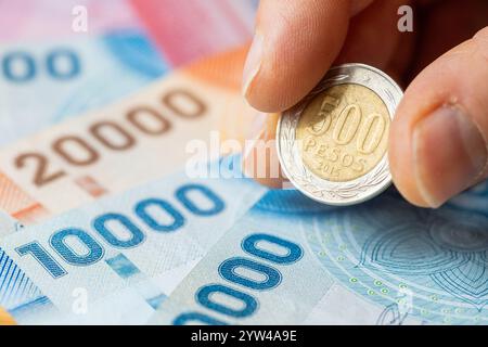 Soldi del Cile. moneta da 500 pesos tenuta nelle dita. Banconote sul tavolo. Concetto di business. Aumento dei risparmi, primo piano Foto Stock