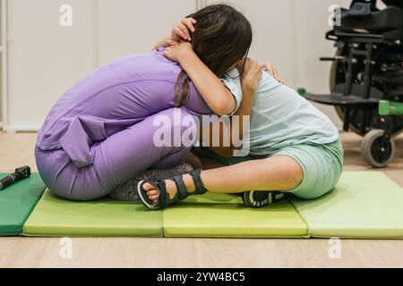 Fisioterapista femminile che abbraccia il bambino con paralisi cerebrale durante la sessione di terapia fisica Foto Stock