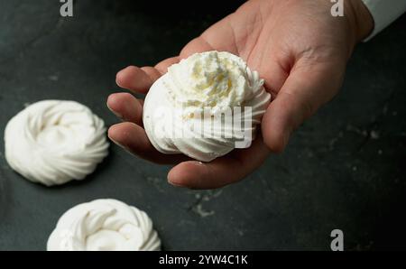Mani che imbettano la panna montata sui nidi di meringa. La superficie a trama scura crea un contrasto rustico con la meringa bianca. Il processo di decorazione di merin Foto Stock
