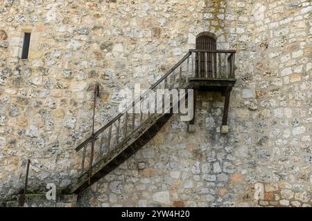 Un primo piano del muro di pietra del castello di Torija, caratterizzato da una scala in legno che conduce a una piccola finestra a cancello, che mostra dettagli architettonici medievali. Foto Stock