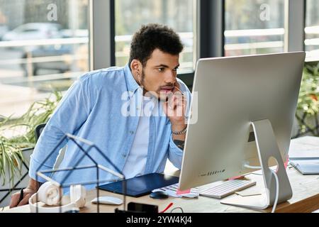 Giovane uomo concentrato sul lavoro a una scrivania elegante, circondato da piante e luce naturale. Foto Stock