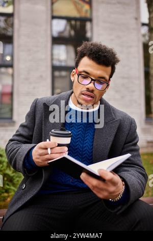 Un bell'uomo riesce a leggere mentre si rilassa all'aperto con una tazza di caffè caldo. Foto Stock