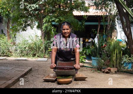 Teotitlan del valle, Oaxaca, Messico; 1 novembre 2024: Un cuoco tradizionale macina il cioccolato su un metate, un antico utensile da cucina per macinare ingre Foto Stock