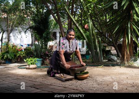 Teotitlan del valle, Oaxaca, Messico; 1 novembre 2024: Un cuoco tradizionale macina il cioccolato su un metate, un antico utensile da cucina per macinare ingre Foto Stock