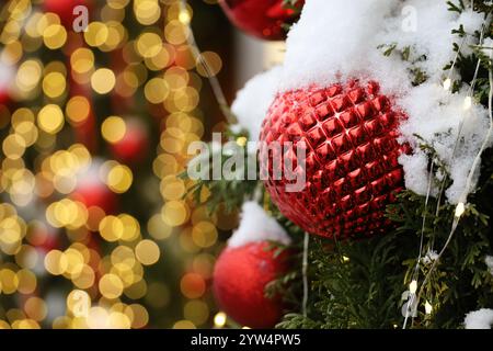 Festa di Capodanno nella città invernale, rami di alberi di Natale con palle rosse ricoperte di neve su sfondo di luci dorate Foto Stock
