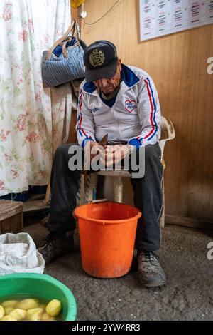 Lurin, Perù - 6 settembre 2024: L'uomo anziano sbuccia le patate su un secchio d'arancia nella cucina della Comunità Foto Stock