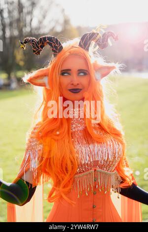 Una bellissima ragazza cosplayer vestita da imperatrice demoniaca della serie di ruoli critici, con un viso e un abbigliamento arancione brillante Foto Stock