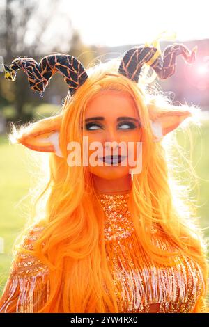 Una bellissima ragazza cosplayer vestita da imperatrice demoniaca della serie di ruoli critici, con un viso e un abbigliamento arancione brillante Foto Stock