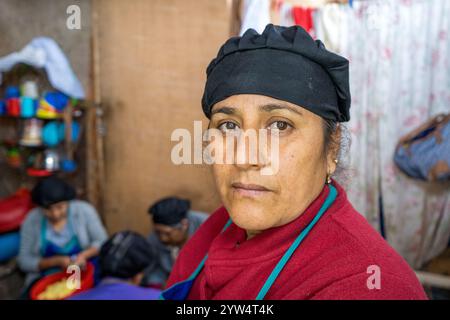 Lurin, Lima, Perù - 6 settembre 2024: Tristezza donna peruviana vestita in rosso con un cappello da cucina nero lavora nella cucina della Comunità Foto Stock