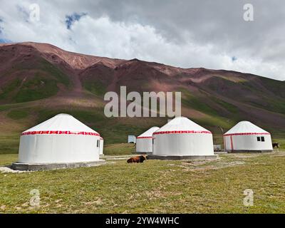 Le yurte tradizionali sono annidate in una valle verde con montagne che si innalzano sullo sfondo in una giornata limpida. Foto Stock