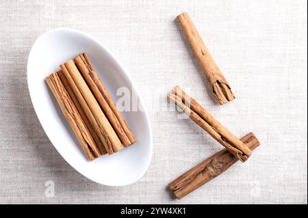 Bastoncini di cannella Ceylon, guanciali di cannella in una ciotola bianca ovale su lino. Gruppo di strisce di corteccia essiccate intere di Cinnamomum verum. Foto Stock