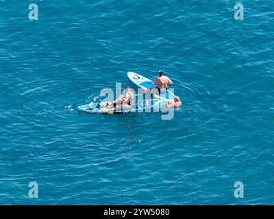 Due donne in mare sedute su tavole SUP con pagaie. Foto Stock