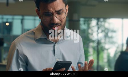 Uomo d'affari indiano Guy uomo d'affari arabo utente maschio visitatore in caffetteria speranza desiderio tenere telefono cellulare ricevere cattive notizie messaggio truffa guasto cellulare Foto Stock