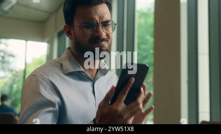 Uomo arabo ragazzo etnico turbato preoccupato frustrato uomo d'affari affari uomo datore di lavoro lavoro lavoratore libero professionista visitatore che legge schermo del telefono cellulare ricevere male Foto Stock