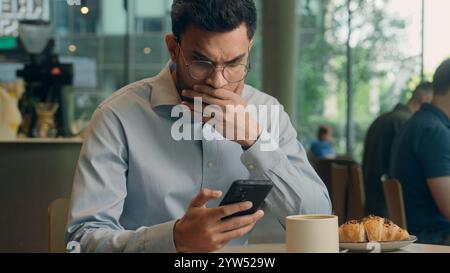 Uomo d'affari indiano Guy uomo d'affari arabo utente maschio visitatore in caffetteria speranza desiderio tenere telefono cellulare ricevere cattive notizie messaggio truffa guasto cellulare Foto Stock