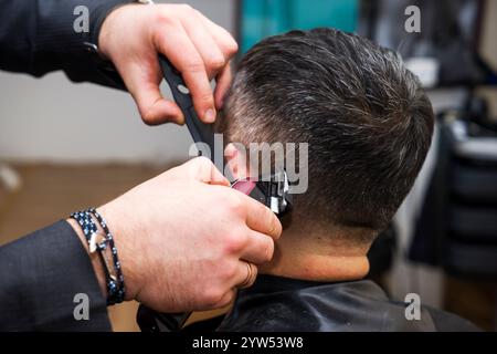 acconciatura e taglio dei capelli da uomo con il regolacapelli in un barbiere o in un parrucchiere, primo piano Foto Stock