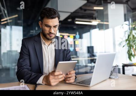 Un professionista aziendale si concentra sul suo tablet in un ufficio moderno, evidenziando la tecnologia e la produttività sul posto di lavoro. Foto Stock